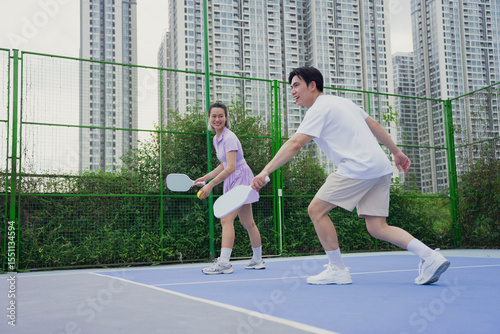 Enjoying pickleball on a sunny afternoon at an urban court surrounded by tall buildings, showcasing friendly competition
