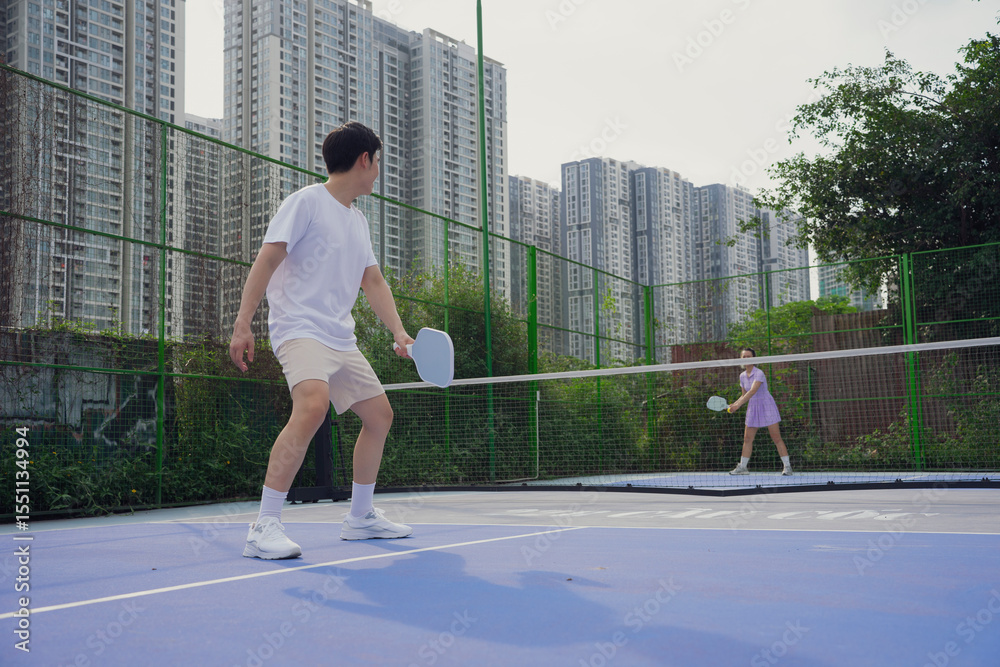 Obraz premium Pickleball match between two players on an urban court surrounded by high-rise buildings during a sunny day