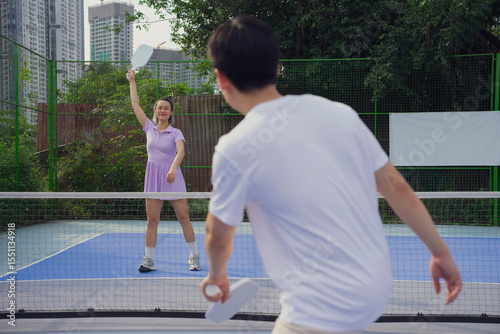 Asian players engaging in competitive pickleball match outdoors in a vibrant urban setting