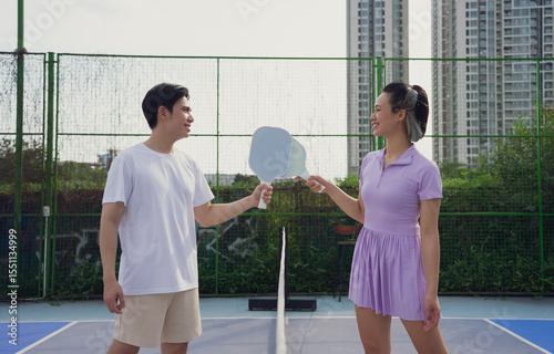 Two players engage in a friendly pickleball match on an outdoor court surrounded by high-rise buildings