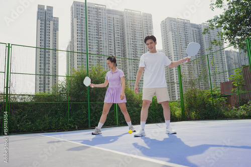 Pickleball players enjoy a sunny day on a court in an urban setting with tall buildings in the background near their city