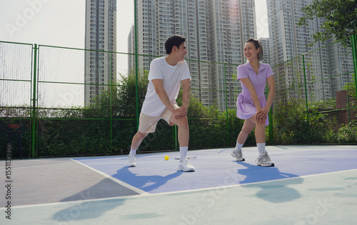 Young Asian adults engage in warm-up exercises on a pickleball court in an urban setting before their game
