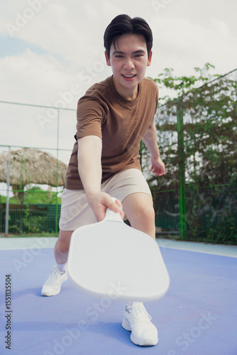 Young man playing pickleball on a sunny day in an outdoor court in Asia, showcasing skill and enthusiasm in a lively game