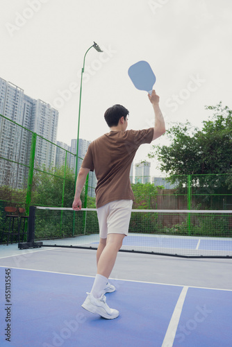 Young athlete prepares to serve in pickleball match at urban sports facility on a sunny day