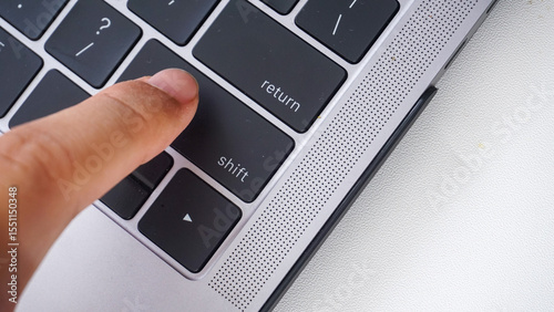 Top view of finger pressing shift button of a laptop keyboard isolated on white background