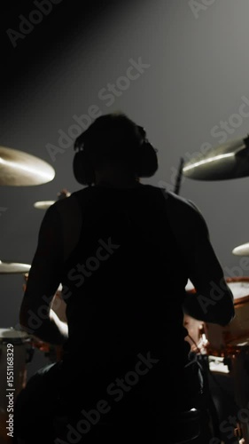 Back view of male person playing drum set, professional rock musician rehearsing alone or performing rock gig. Brawny man striking drums and cymbals, rear view, feel energy and power of modern music