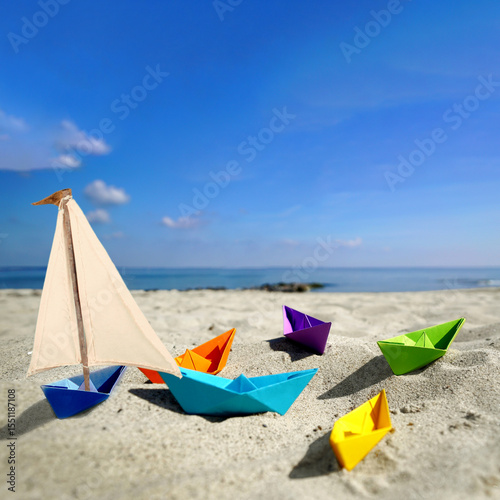 Whimsical Summer Delight: Colorful Paper Boats Resting on Sandy Shores with the Sparkling Sea and Sunshine in the Background