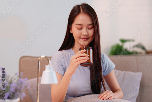 Young Asian woman enjoying soothing aromatherapy with scented candle for relaxation and stress relief enhancing home wellness and peaceful longevity lifestyle