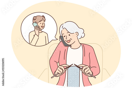 Grandmother makes phone call to granddaughter and knits scarf sitting in cozy chair