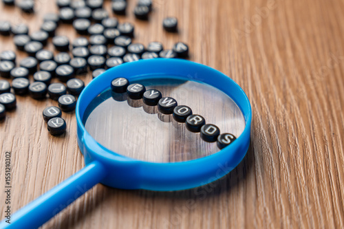 A blue magnifying glass with alphabet beads that spell out KEYWORDS. Searching, optimization, discovery, SEO, data, and online content concept.