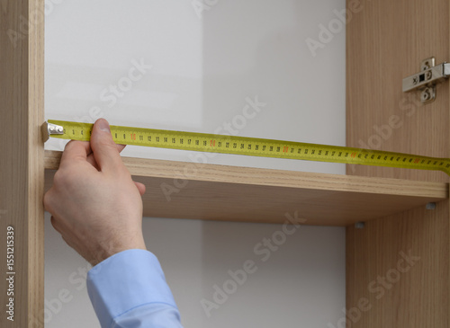 A carpenter makes a custom-made wardrobe, measuring the length of the shelf with a ruler