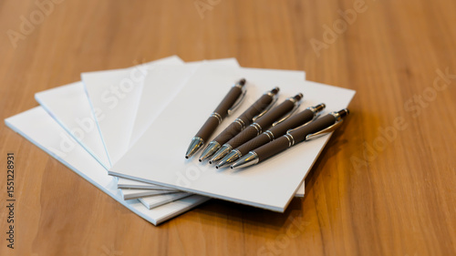 Notepad for agenda kept with pens on the desk in empty corporate conference room before business meeting concept.