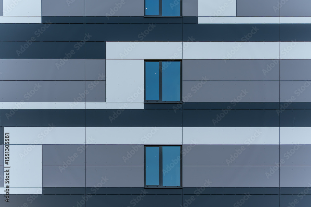 Detailed view of a modern house facade with gray and white surfaces. Three windows stand out against the strict geometry Detailed view of a modern house facade with gray and white surfaces. Three windows stand out against the strict geometry
