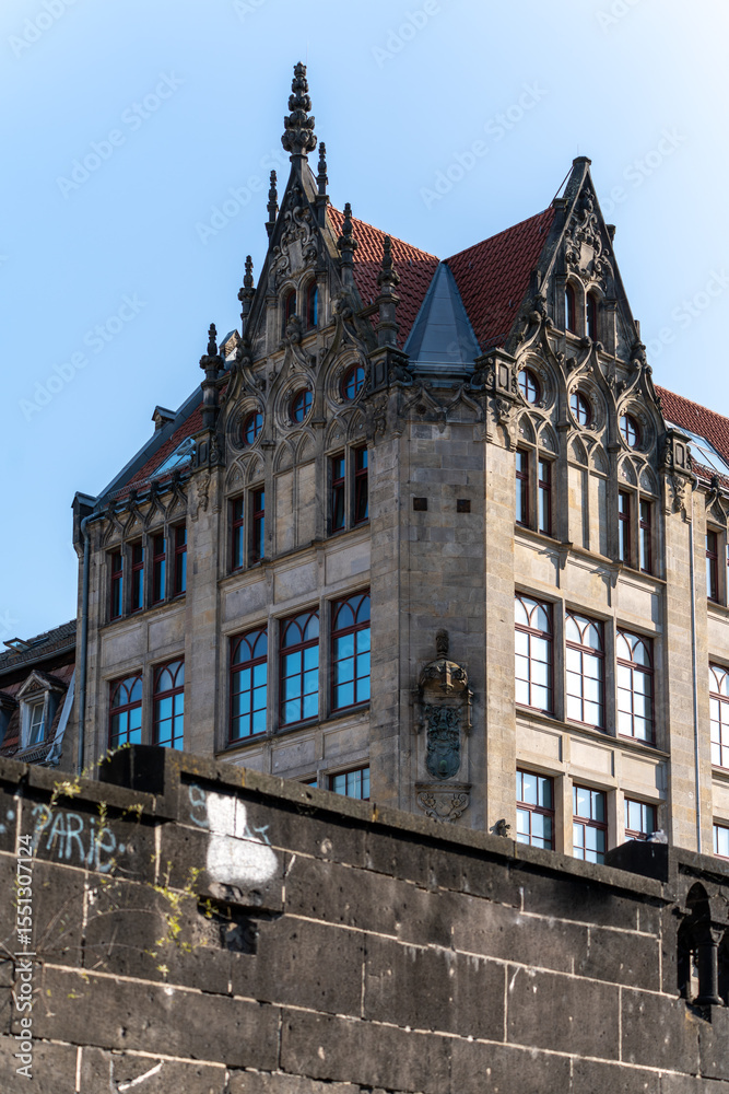 Fototapeta premium An elaborately designed historic building with red roofs and pointed gables rises into the blue sky. The facade is richly decorated with ornaments and coats of arms.