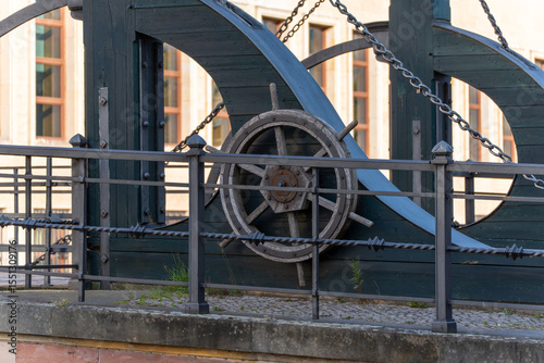 A wooden steering wheel is part of an old technical device with chains and metal rods. Historical craftsmanship meets functional design.