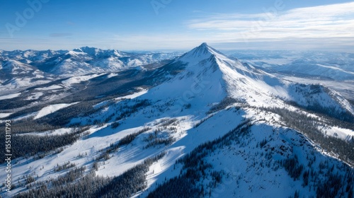 Majestic snowcovered mountain peak surrounded by rugged ridges and dense pine forests under a clear winter sky with long shadows and glistening snow.