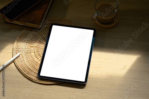 Digital tablet with blank screen on wooden desk beside coffee cup in soft morning light