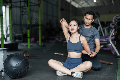 Personal Training and Fitness Coaching. A trainer assisting a woman with stretching exercises in a gym.