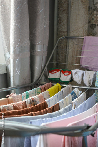 colorful clothes drying on metal rack indoors near window, symbol of home routine, laundry day, household chores, cleanliness, domestic life, family care, eco lifestyle