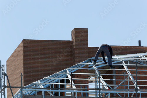 Hombre trabajando sin protección en la estructura del tejado de un edificio. photo