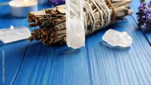 Close-up of healing crystals, smudge stick, candle and lavender flowers on a textured blue wooden surface for spiritual rituals.