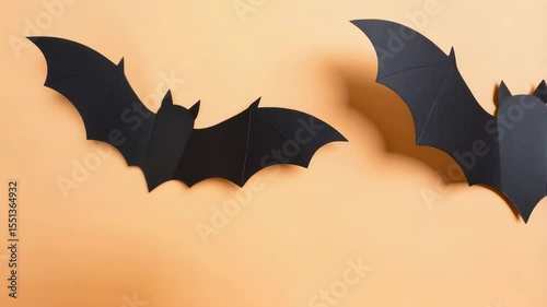 Two black paper bats on light orange background. Halloween decorations, spooky animals, scary holiday concept. Flat lay, copy space for text.