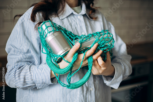 Woman in kitchen holding mesh bag with empty used cans, recycling at home.