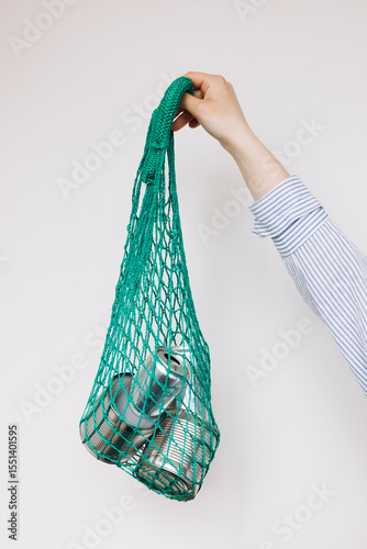 Cans in green mesh bag on white background, recycling and eco-friendly concept.