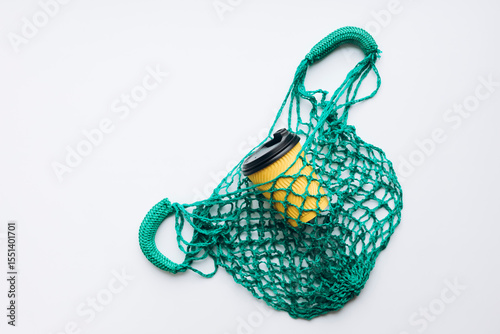 Flat lay yellow disposable paper cup in green mesh bag on white background.