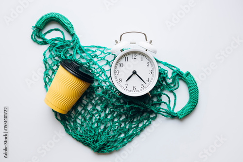 Flat lay composition with alarm clock, mesh bag, and paper cup on white.