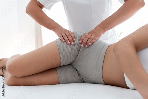 Hands of osteopath treating teenage patient's hip on massage table at rehabilitation center photo