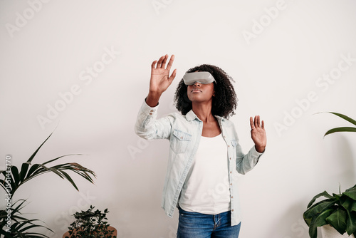Woman wearing virtual reality headset standing in front of white wall at home