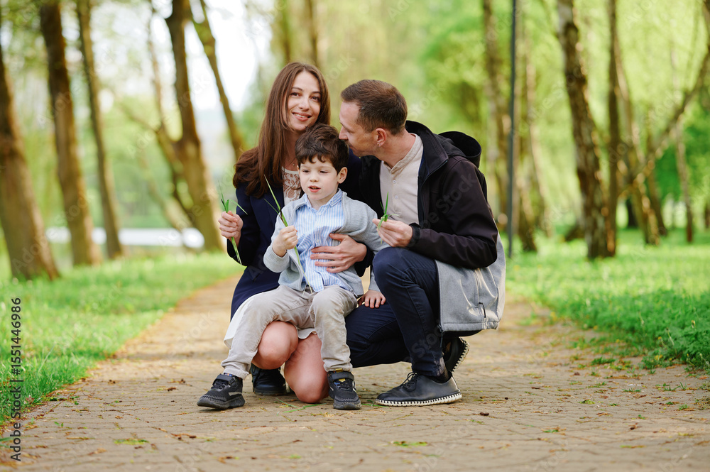 Fototapeta premium happy family enjoying time outdoors. smiling parents and child seated together on tree-lined path in green park, conveying warmth, happiness, and togetherness on a sunny day