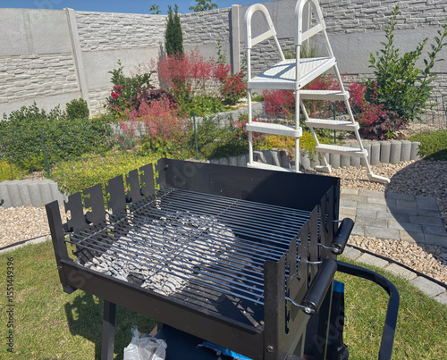 Empty charcoal barbecue grill with fresh ash in a sunny backyard garden, concept of outdoor cooking, summer entertaining, home leisure