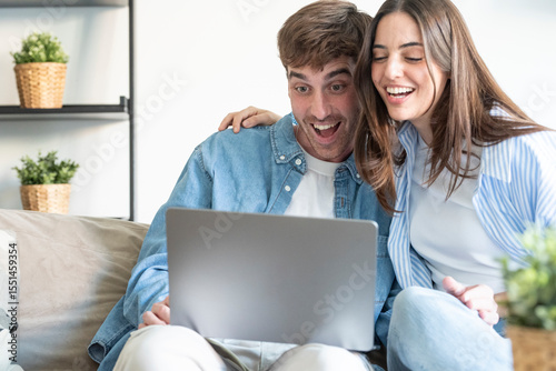 Excited young couple celebrating great news in front of laptop at home. Joyful reaction after receiving a positive email or notification about a win, pregnancy, online auction or exam results. Real ha