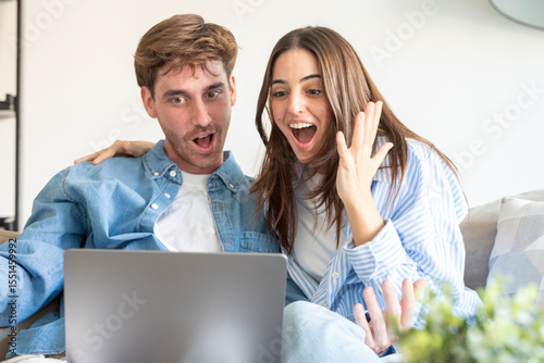 Excited young couple celebrating great news in front of laptop at home. Joyful reaction after receiving a positive email or notification about a win, pregnancy, online auction or exam results. Real ha