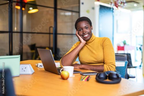Smiling businesswoman leaning on elbow sitting at desk in office