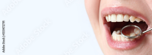Smiling woman at the dentist, close-up. Dental mirror. Dentist examines patient's teeth with a dental mirror. Dentistry and oral hygiene concept. Real white teeth, not veneers. Close-up of teeth