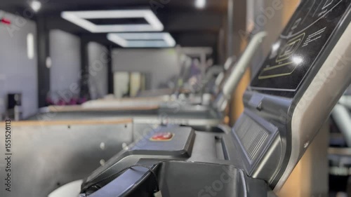 A low angle, close-up capturing a row of sleek treadmills with illuminated displays inside a contemporary fitness studio. The blurred background indicates a place dedicated to physical activity.