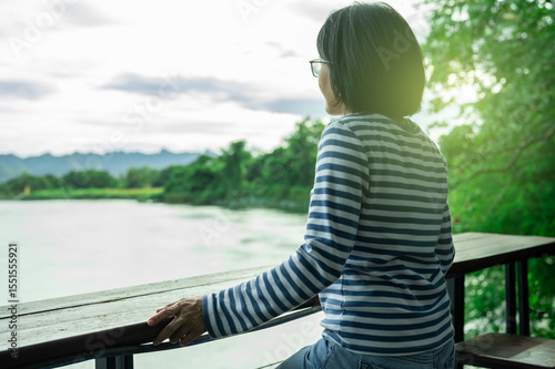Rear view of a woman gazing at calm river. Travel retreat. Peaceful solitude, personal reflection. Nature connection. Freedom, and emotional healing. Rest, and inner clarity. Emotional balance.