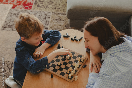 Wallpaper Mural Happy mother playing chess with her 7-year-old son at home. Concept of childhood development, quality time, strategy, and joyful parenting in a cozy home environment. Torontodigital.ca