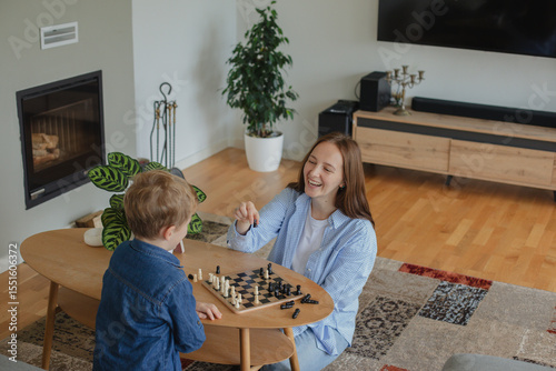 Wallpaper Mural Happy mother playing chess with her 7-year-old son at home. Concept of childhood development, quality time, strategy, and joyful parenting in a cozy home environment. Torontodigital.ca