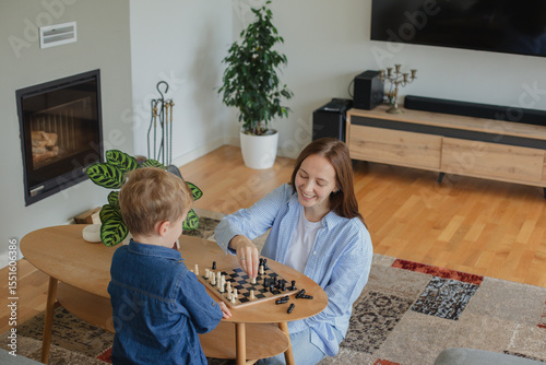 Wallpaper Mural Happy mother playing chess with her 7-year-old son at home. Concept of childhood development, quality time, strategy, and joyful parenting in a cozy home environment. Torontodigital.ca