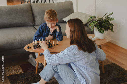 Wallpaper Mural Happy mother playing chess with her 7-year-old son at home. Concept of childhood development, quality time, strategy, and joyful parenting in a cozy home environment. Torontodigital.ca