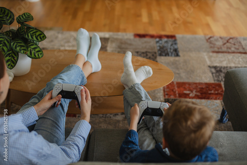 Wallpaper Mural A cheerful mother and her young son sitting on a cozy couch, fully immersed in playing video games together. Torontodigital.ca