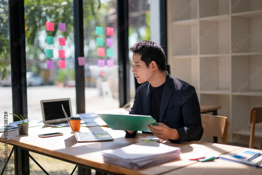 A man is sitting at a desk with a green folder in his hand A man is sitting at a desk with a green folder in his hand