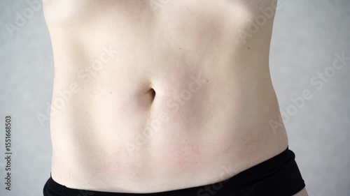 Closeup of a young caucasian female twisting midsection with gray background in slow motion capturing movement and skin detail.