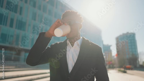 Medium portrait of handsome african american man with coffee cup in city center. Self-confident businessman walking alone on street, move to goal and dream about future win, modern urban landscape
