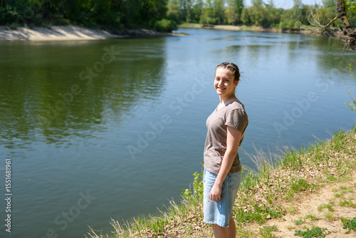 Teen girl walking along the river bank, beautiful spring nature in the forest, green leaves, landscape