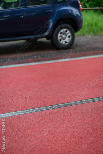 Wallpaper Mural Red material on asphalt with a white dividing line in the center and parts of a blue car in the background after rain. 
 Torontodigital.ca